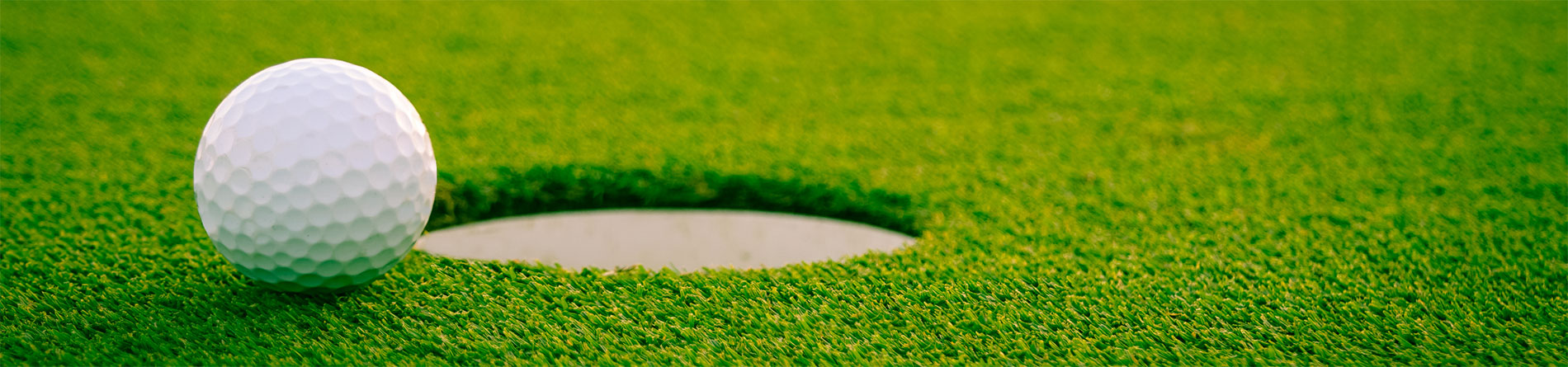 White golf ball on a green, just inches from the golf hole.