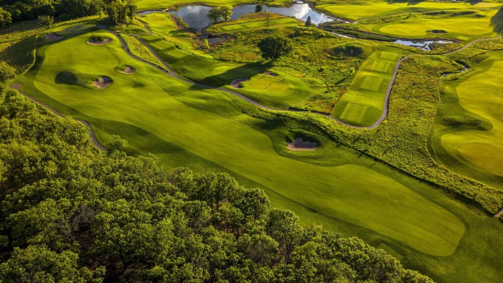 Aerial view of a sprawling green golf course with fairways, bunkers, cart paths, water hazards, and dense trees.