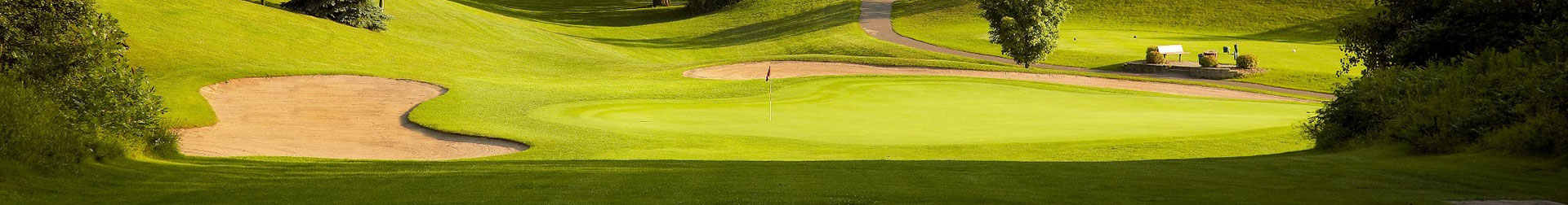 Golf green with a red flag, large sand bunker, rolling hills, and a winding cart path.