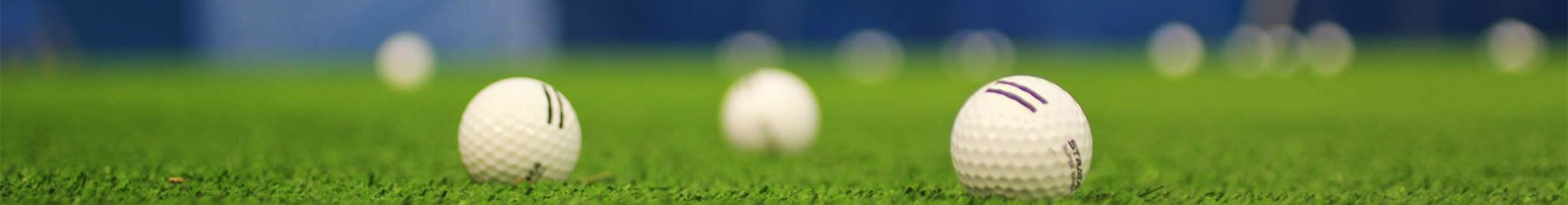 Two golf balls, one with black stripes and one with purple stripes, on artificial green turf, with more balls blurred behind.