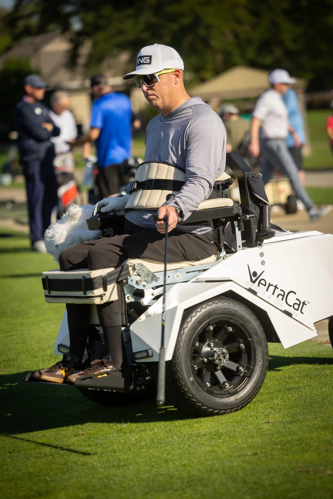 Man in a white VertaCat adaptive golf cart holding a club on the fairway.