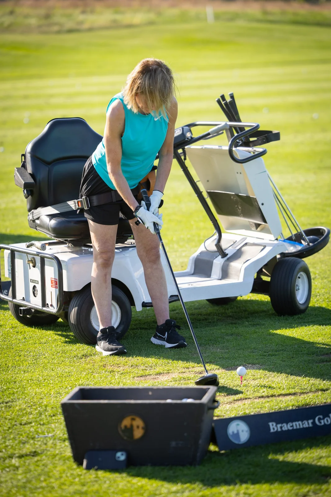 Golfer in teal top with an adaptive golf cart teeing up a ball at Braemar Golf Course.