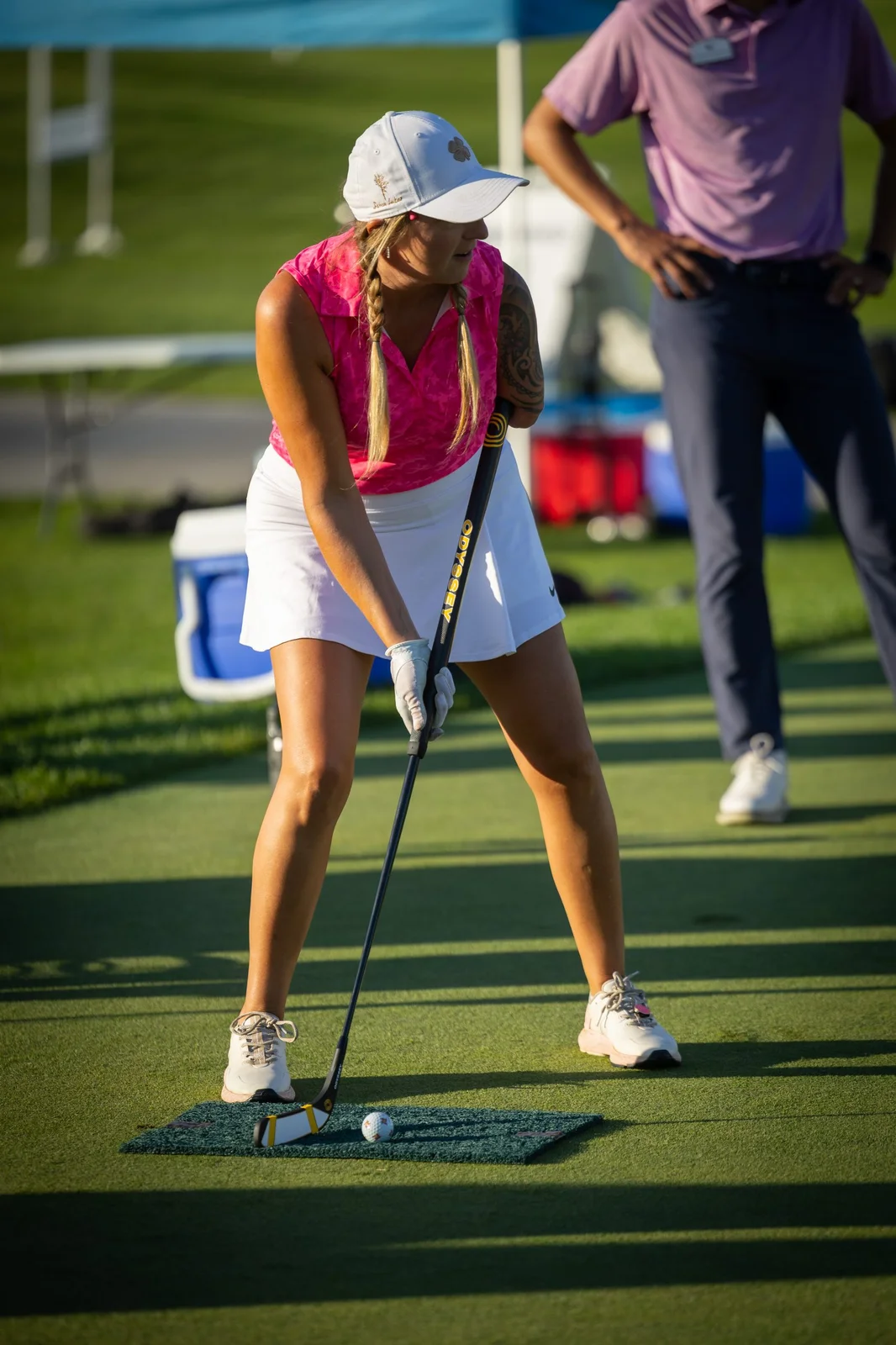 Woman in pink shirt and white skirt putting golf ball on a green practice mat.