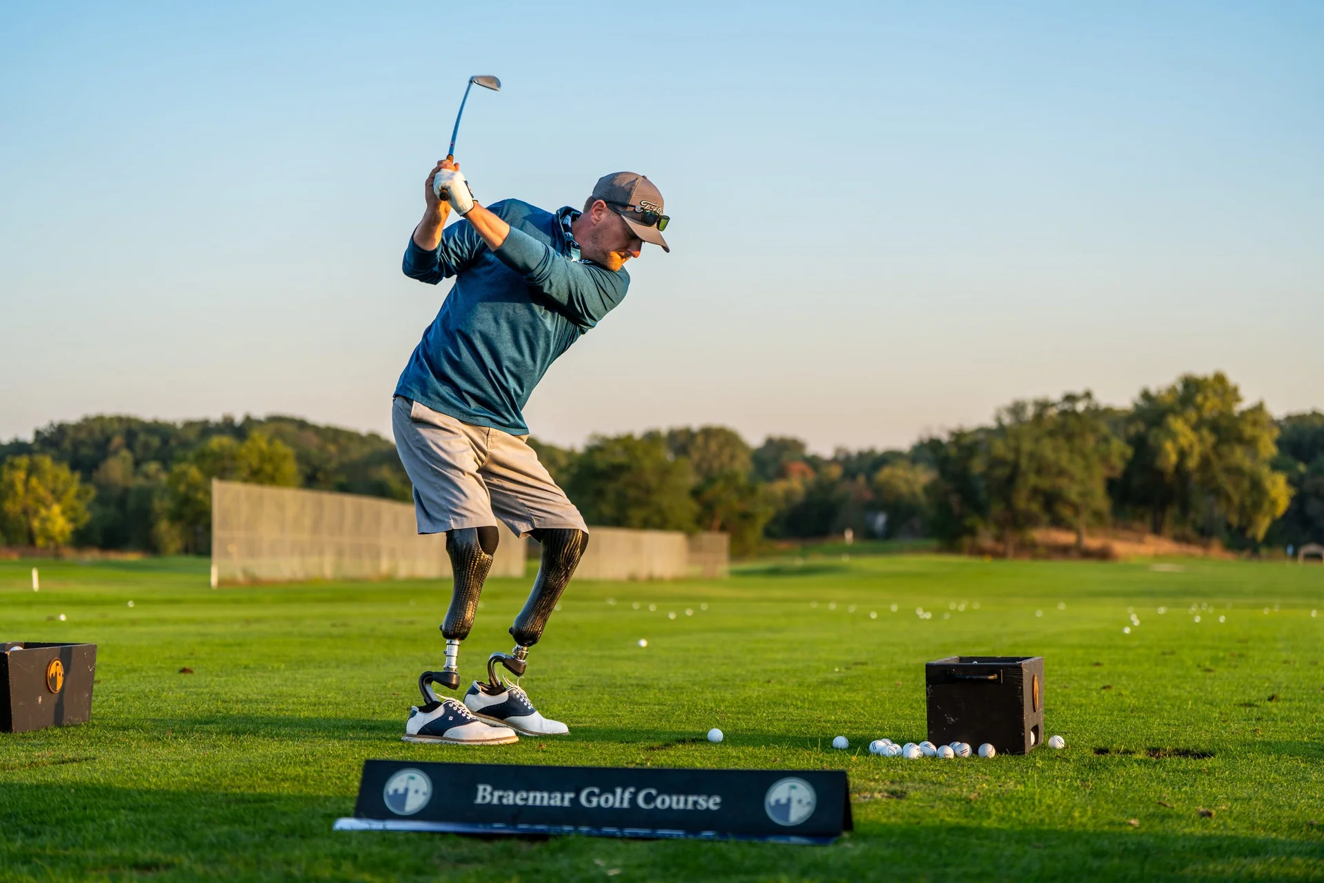 Golfer with prosthetic legs in mid-swing on the driving range at Braemar Golf Course.