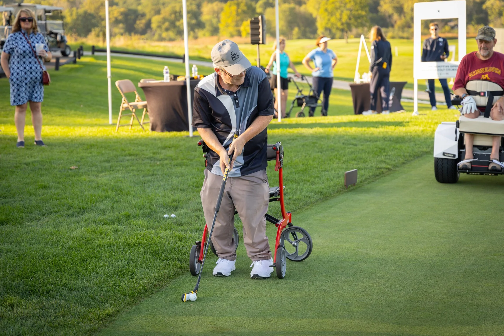 Golfer uses a red wheeled adaptive walker to putt on a sunny green during an event.