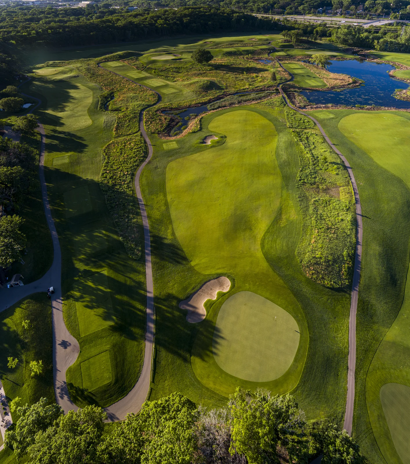 Aerial view of a sprawling golf course with multiple green fairways, bunkers, water hazards, and winding cart paths.