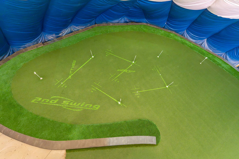 High-angle wide shot of an indoor golf dome putting green equipped with PuttView projection graphics, target lines, and multiple hole locations.