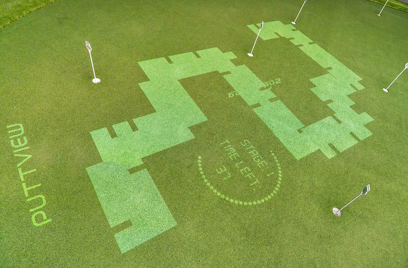 Overhead view of an indoor green featuring a projected interactive PuttView game path with dynamic light patterns and text reading "Stage 1" and "Time Left".